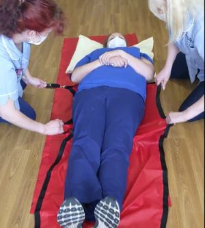 Carers utilising a strain gauge while sliding a colleague using transfer sheets on a hospitals floor. Part of an experiment into effort required to move a patient on different surfaces.